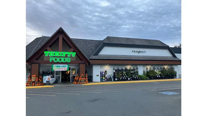 Bright Thrifty Foods grocery store exterior with a pharmacy and vibrant outdoor plants, inviting under a dramatic cloudy sky.